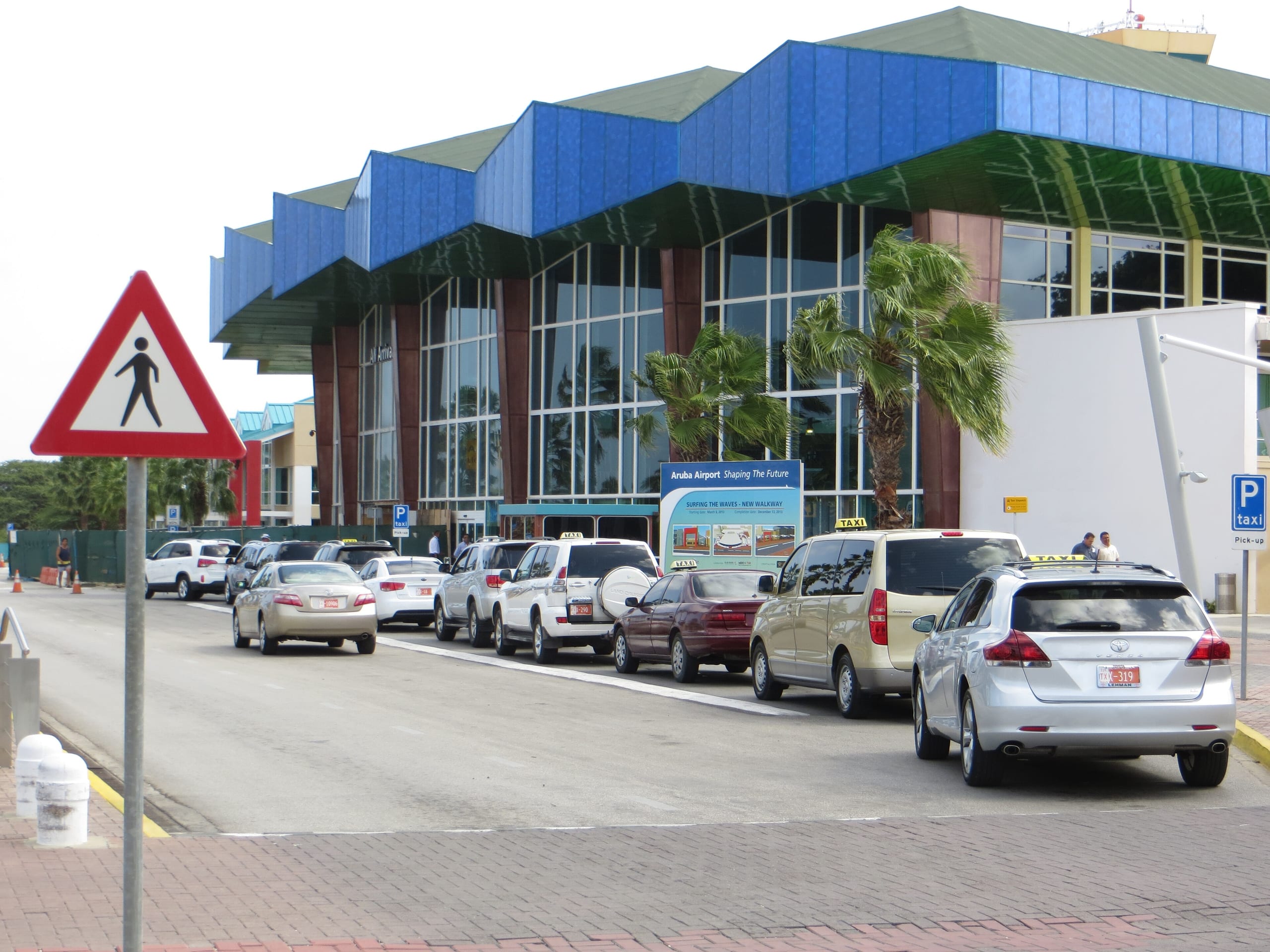 A line of taxis with roof signs waiting at the curb outside the arrivals building at Queen Beatrix International Airport, Aruba