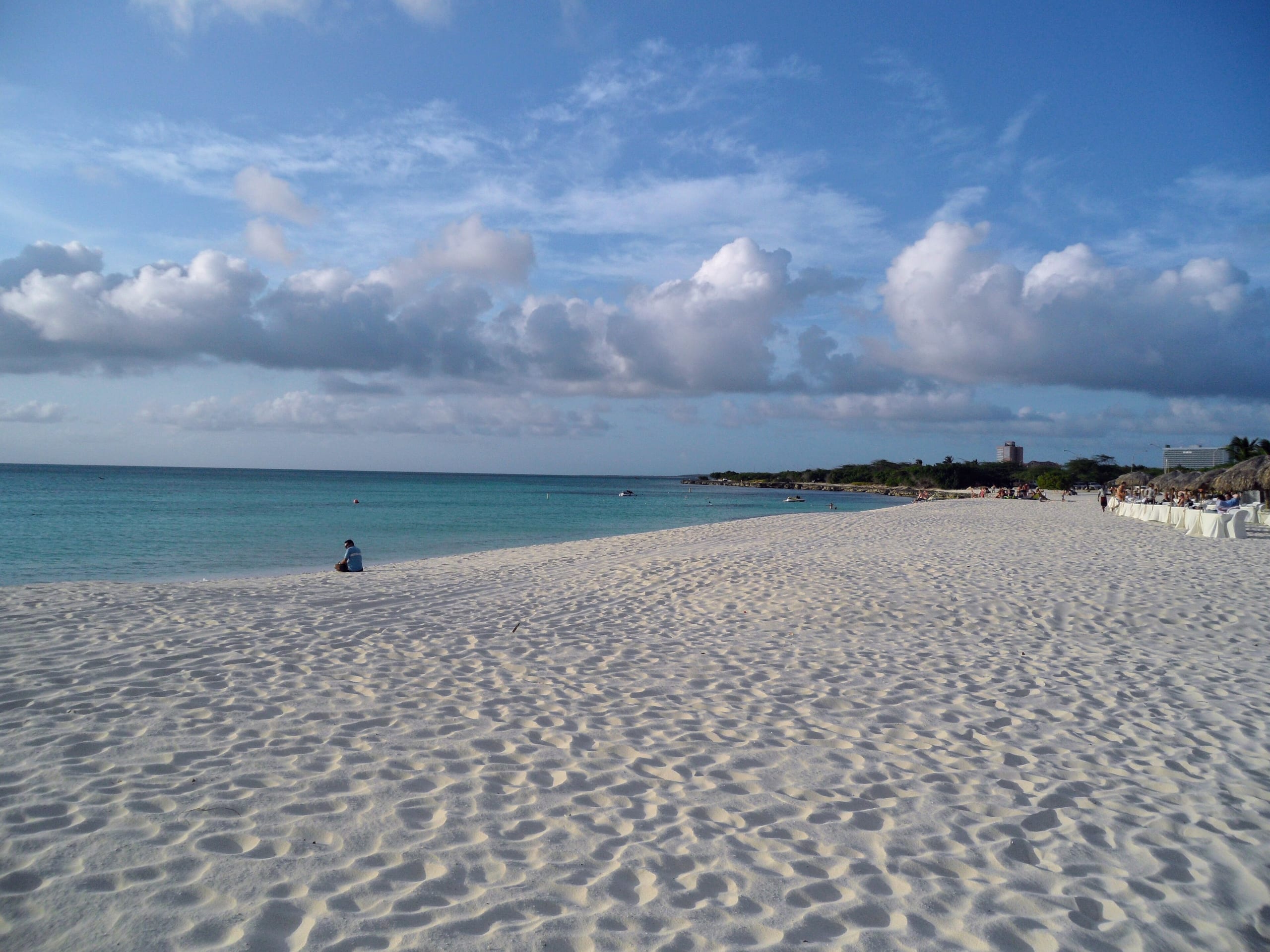Wide white sand and turquoise water at Eagle Beach, Aruba, with a beach restaurant set up under thatched umbrellas on the right