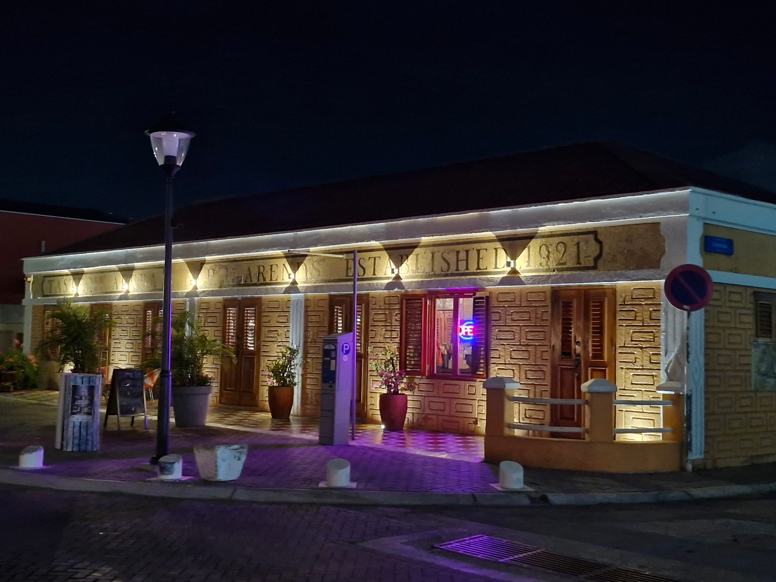 The lit facade of the Taste My Aruba restaurant on Wilhelminastraat, Oranjestad, Aruba, at night, an Open sign glowing in the window