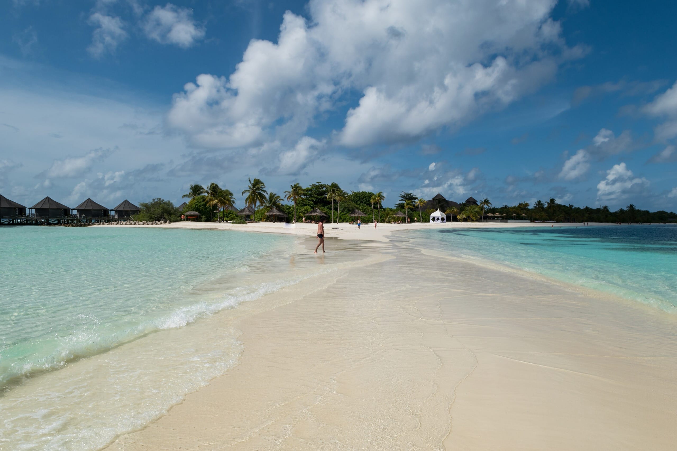A white sandbar in the Maldives with turquoise water on both sides and a resort beyond