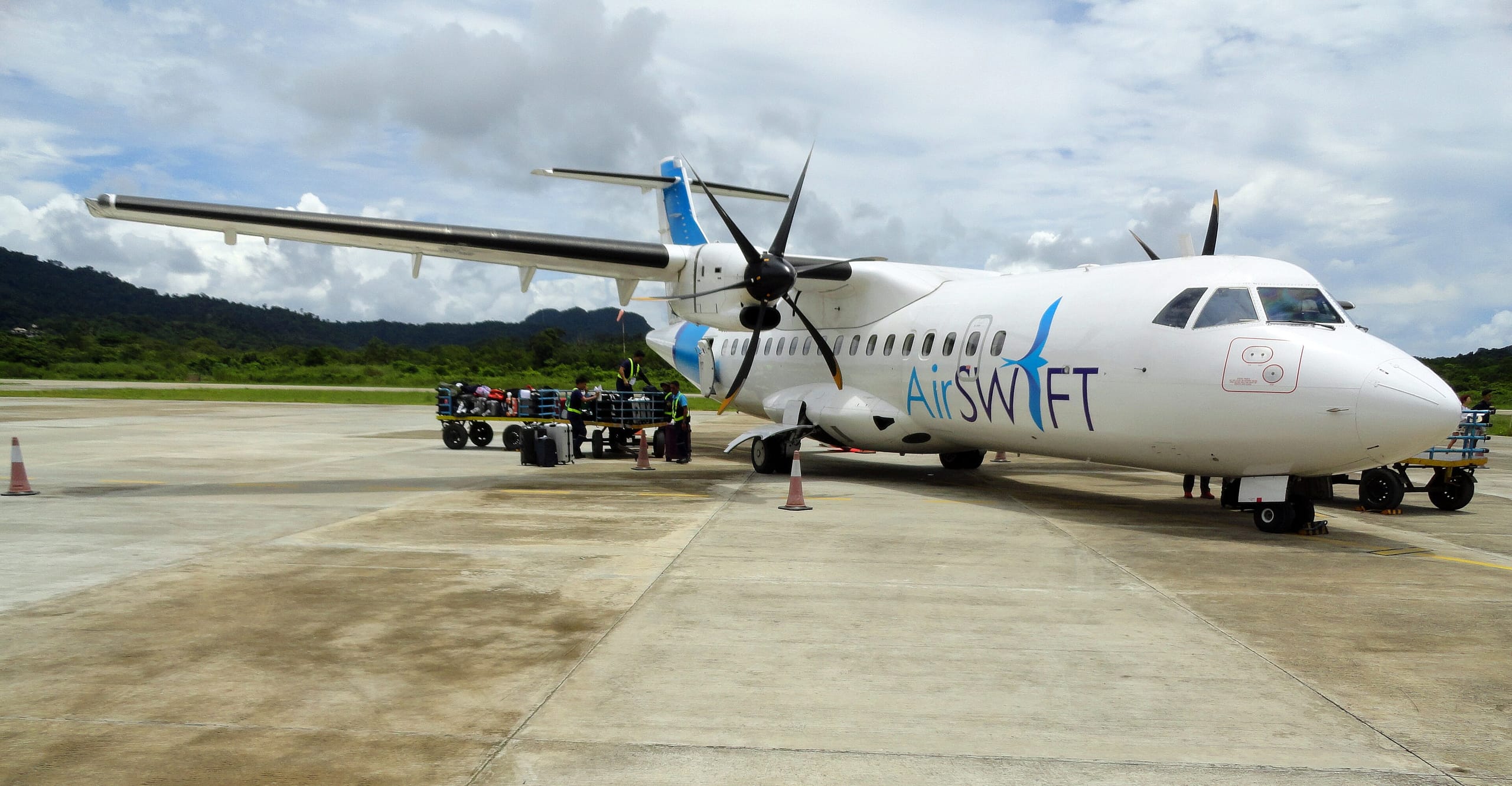 An AirSWIFT turboprop parked on the apron at El Nido airport while ground staff load luggage carts