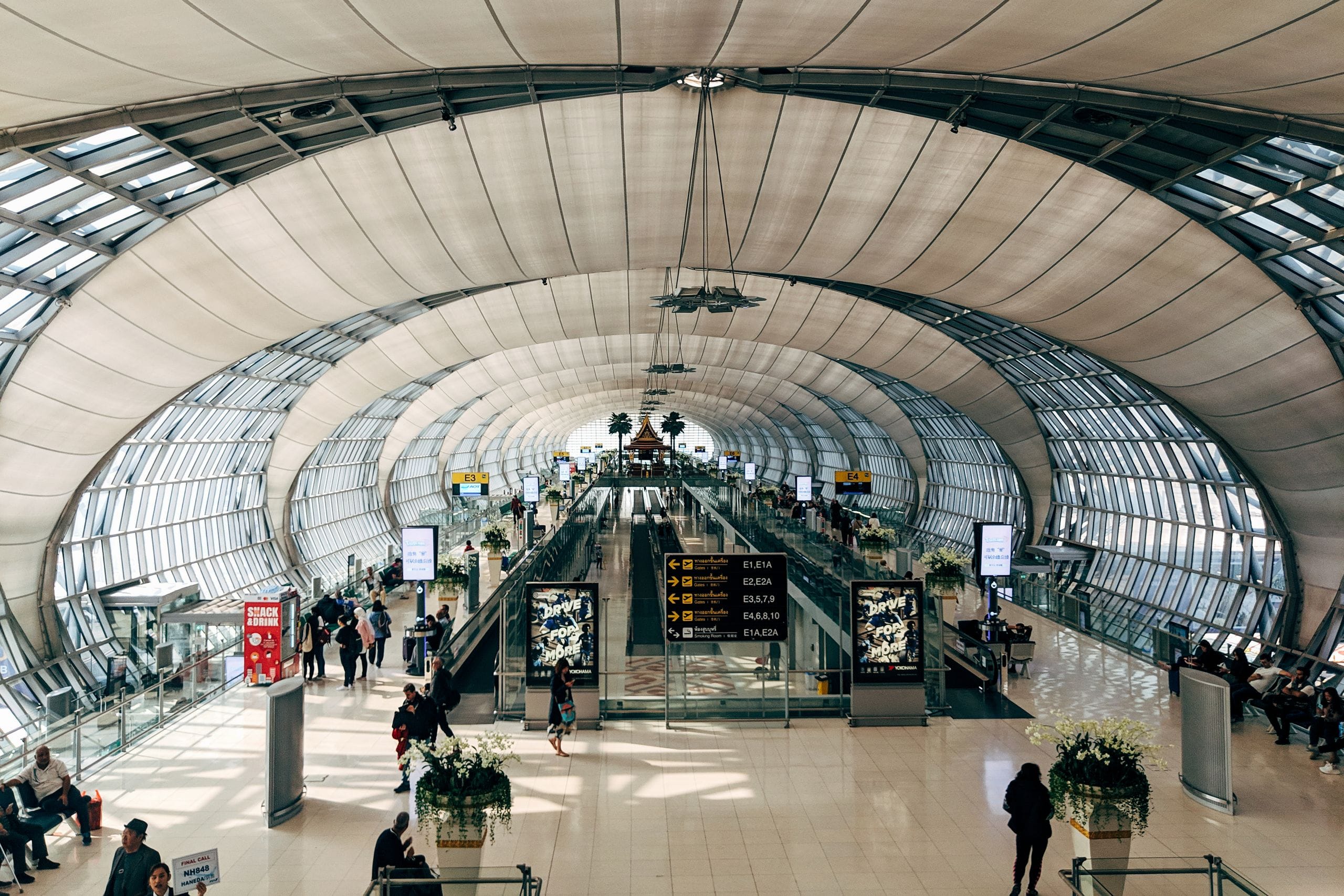 A vaulted glass airport hall at Suvarnabhumi in Bangkok with travelers heading toward the gates