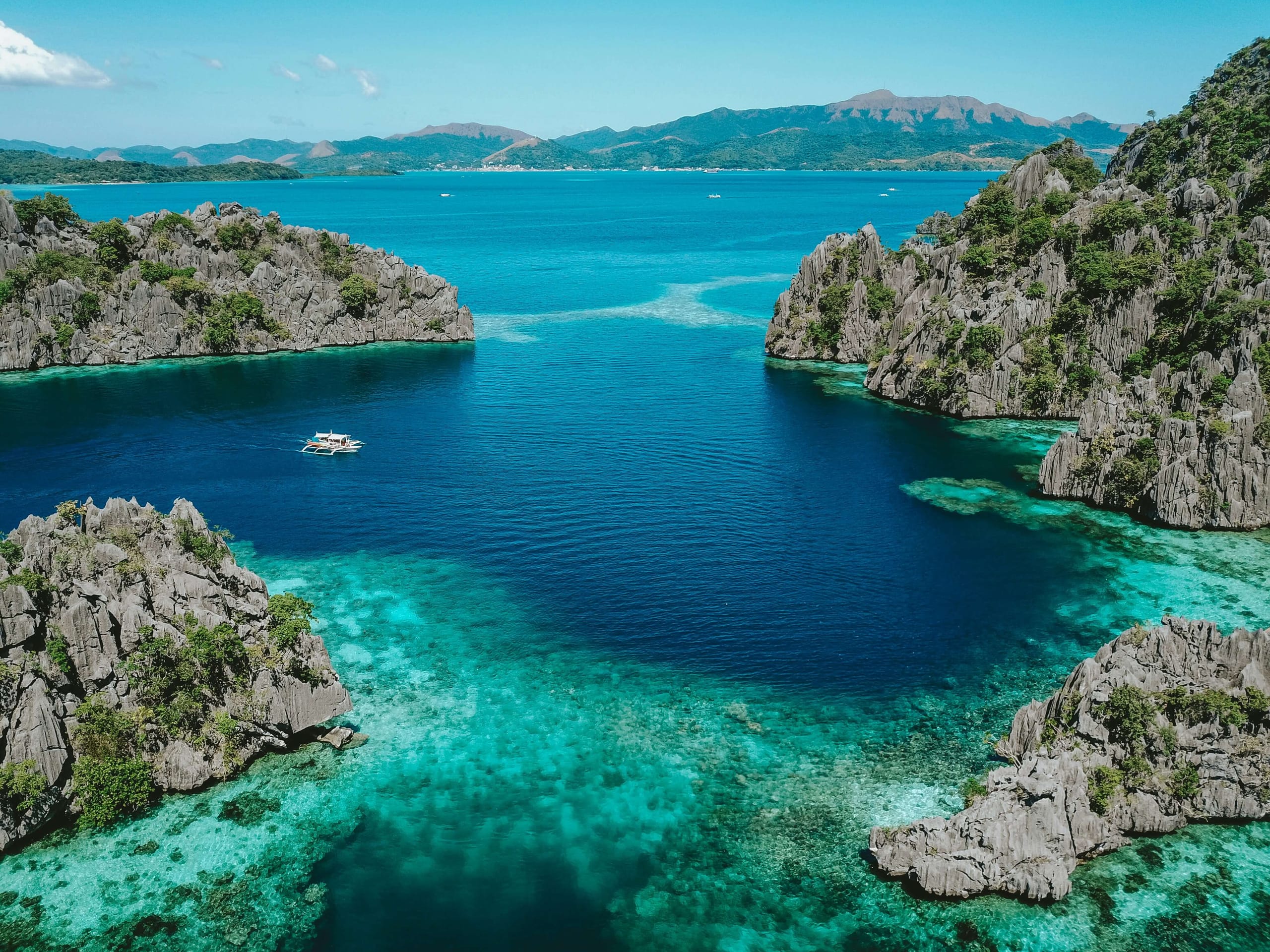Limestone islands enclosing a deep turquoise bay seen from above, dark reef showing under the shallows