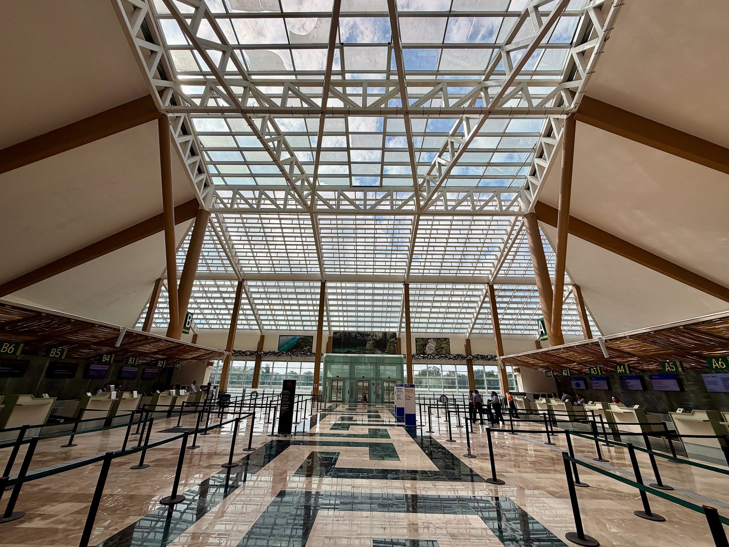 Empty check-in hall at Tulum airport under a glass roof with queue barriers