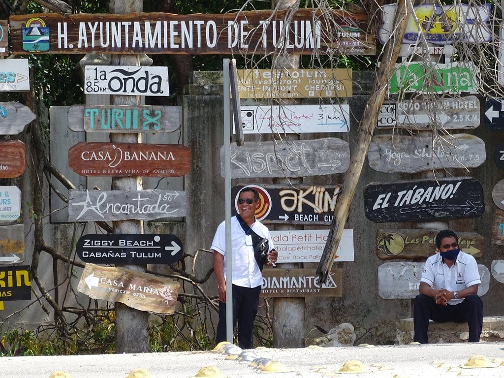 A cluster of hand-painted hotel and beach club signs on a post in Tulum, Quintana Roo
