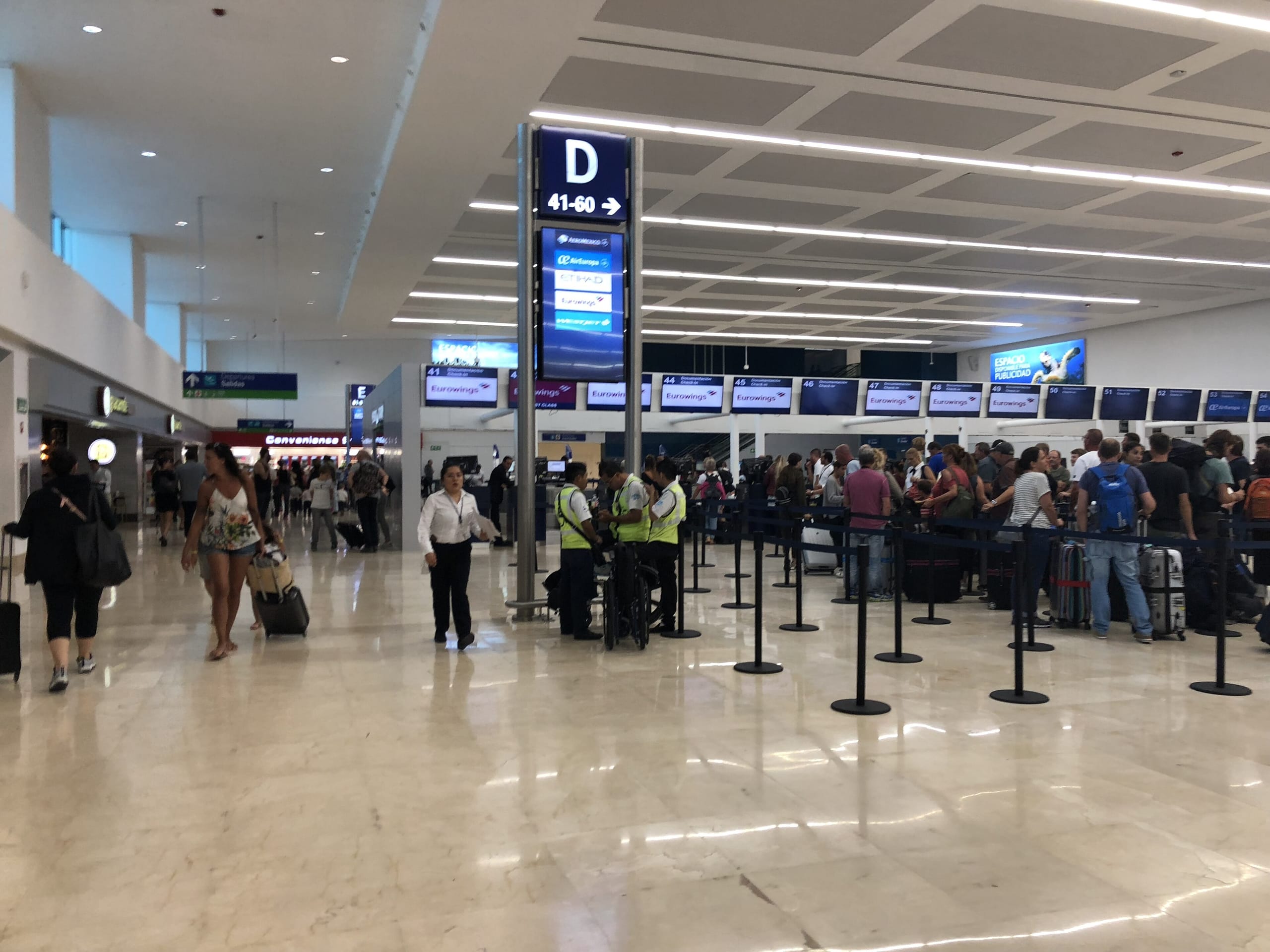 Passengers queue at the check-in counters in a Cancun airport terminal hall