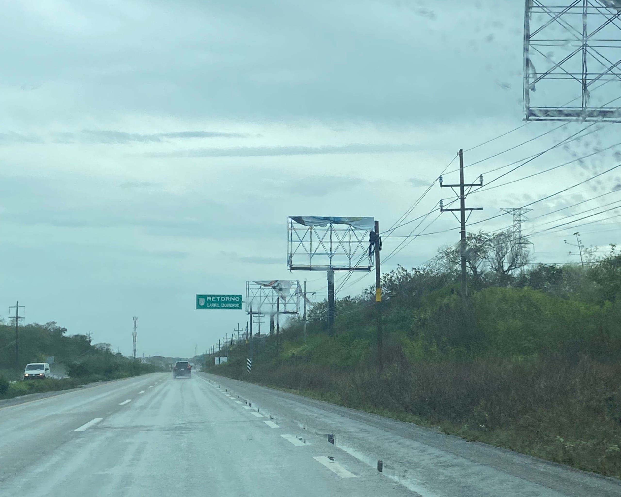 Wet divided highway under grey cloud with billboards and a retorno sign along the Riviera Maya