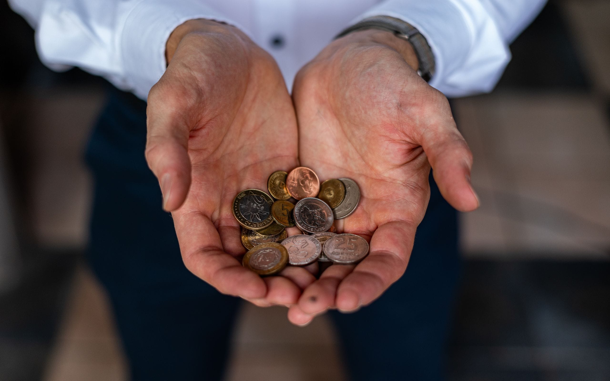 Two open hands holding a small pile of Argentine peso coins in different sizes and colors