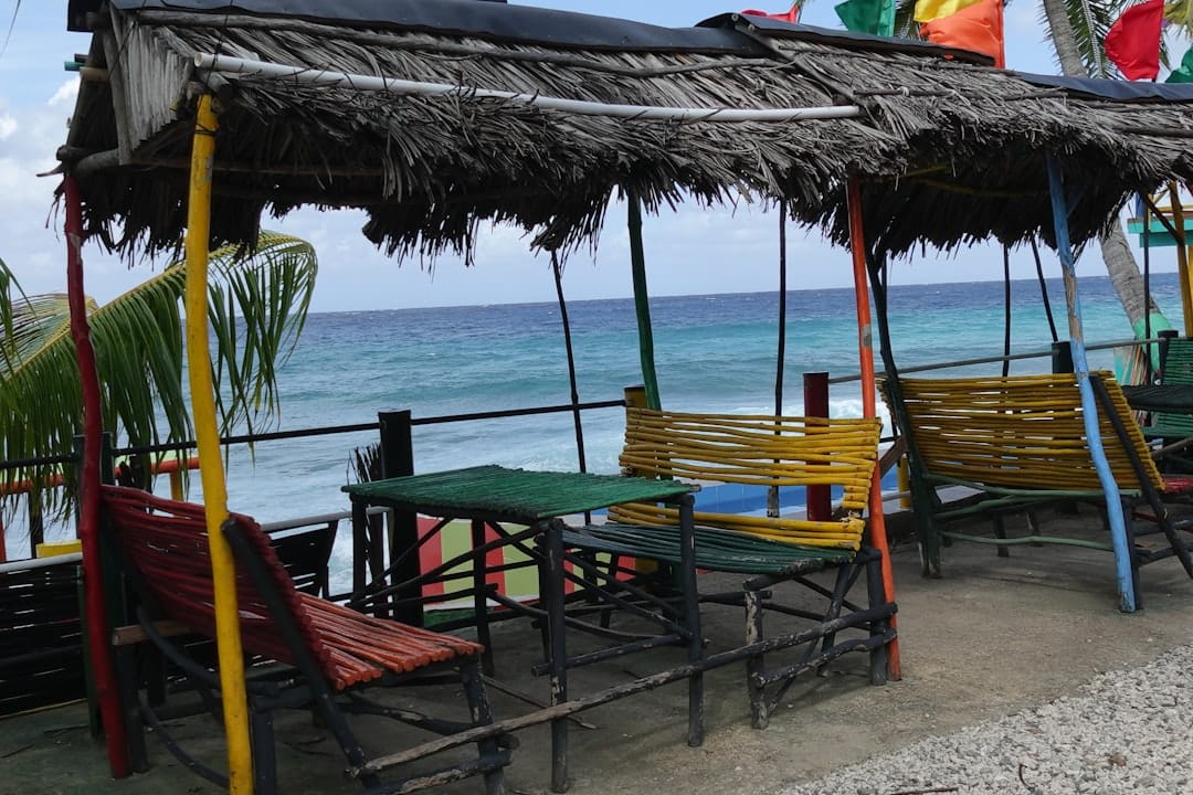 An open-air beach shack under a thatched roof with painted bamboo benches and tables, the sea just beyond the rail
