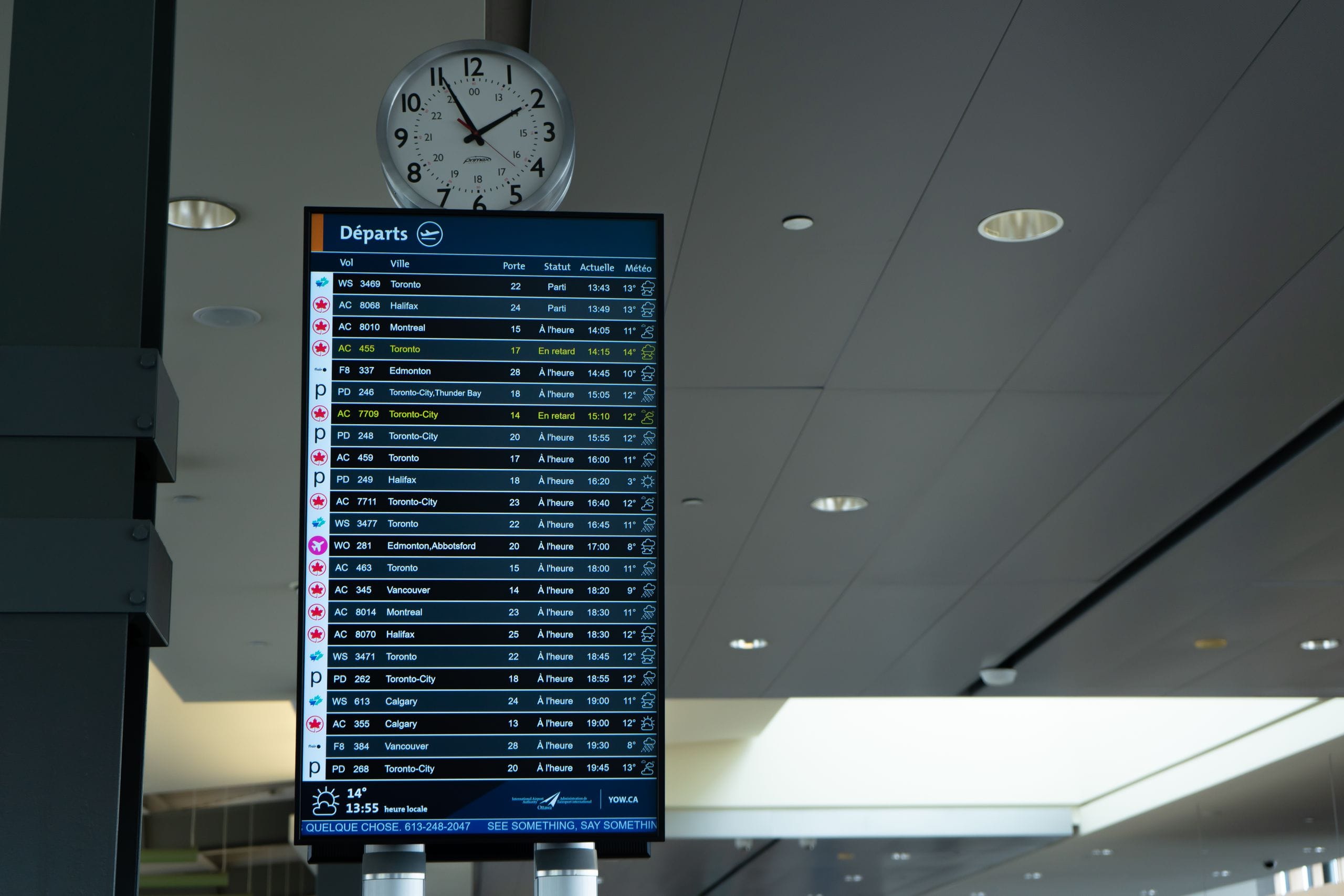 An airport departures screen under a wall clock, two Toronto flights flagged as delayed in yellow