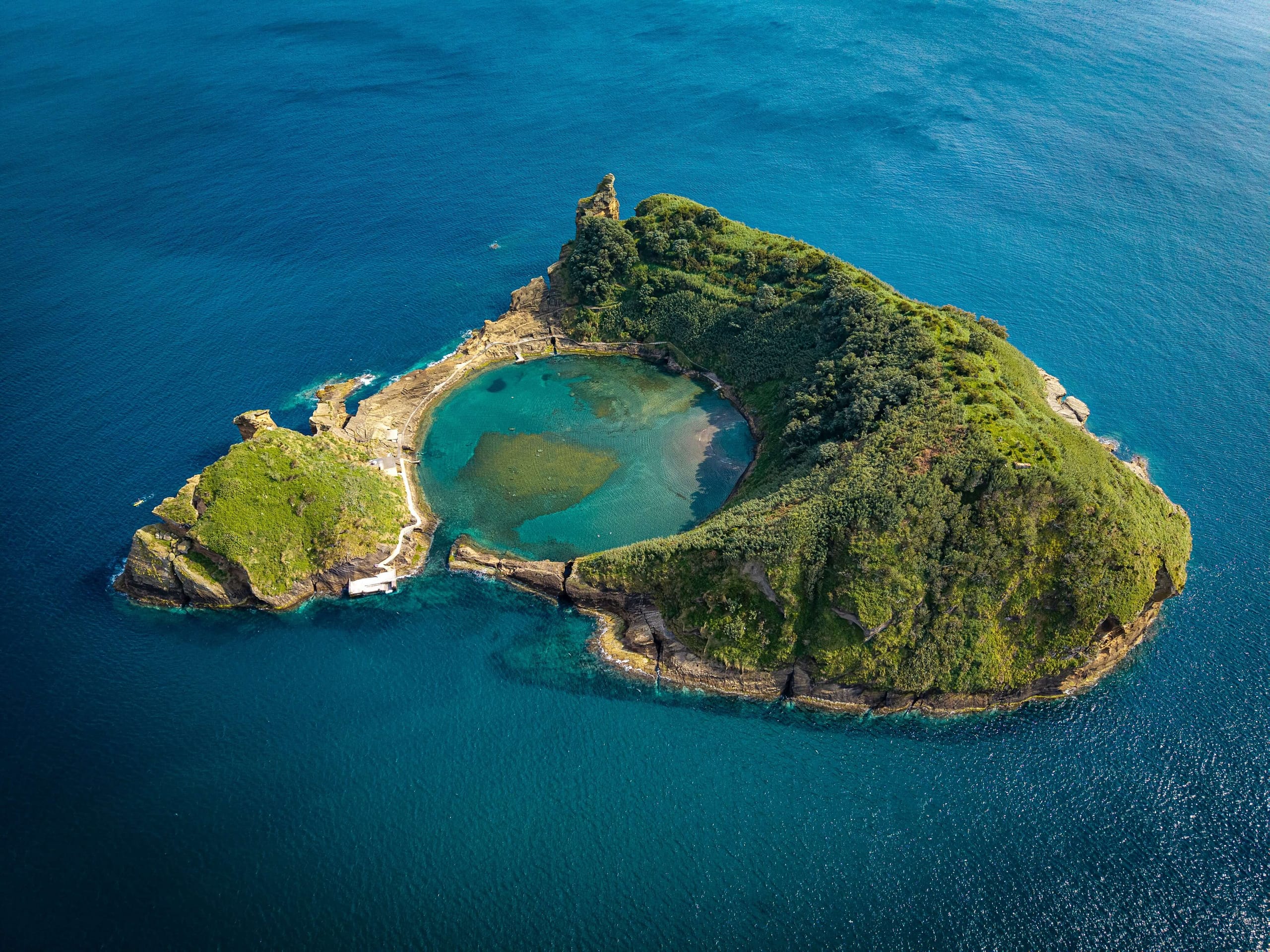 The crater islet of Vila Franca do Campo off the Azores seen from the air, a near-circular ring of green rock with a round lagoon open to the sea inside it