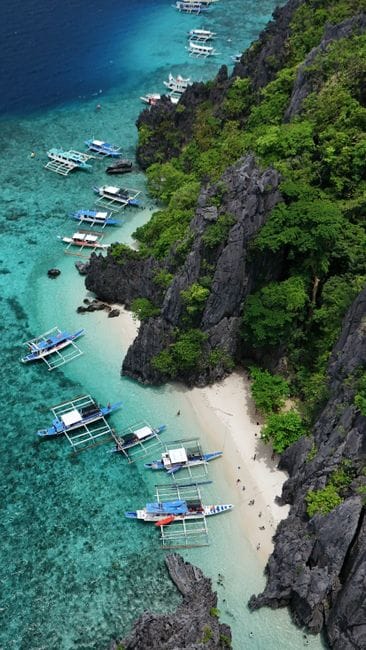 Outrigger boats along a rocky tree-covered shoreline at Coron in Palawan, seen from the air