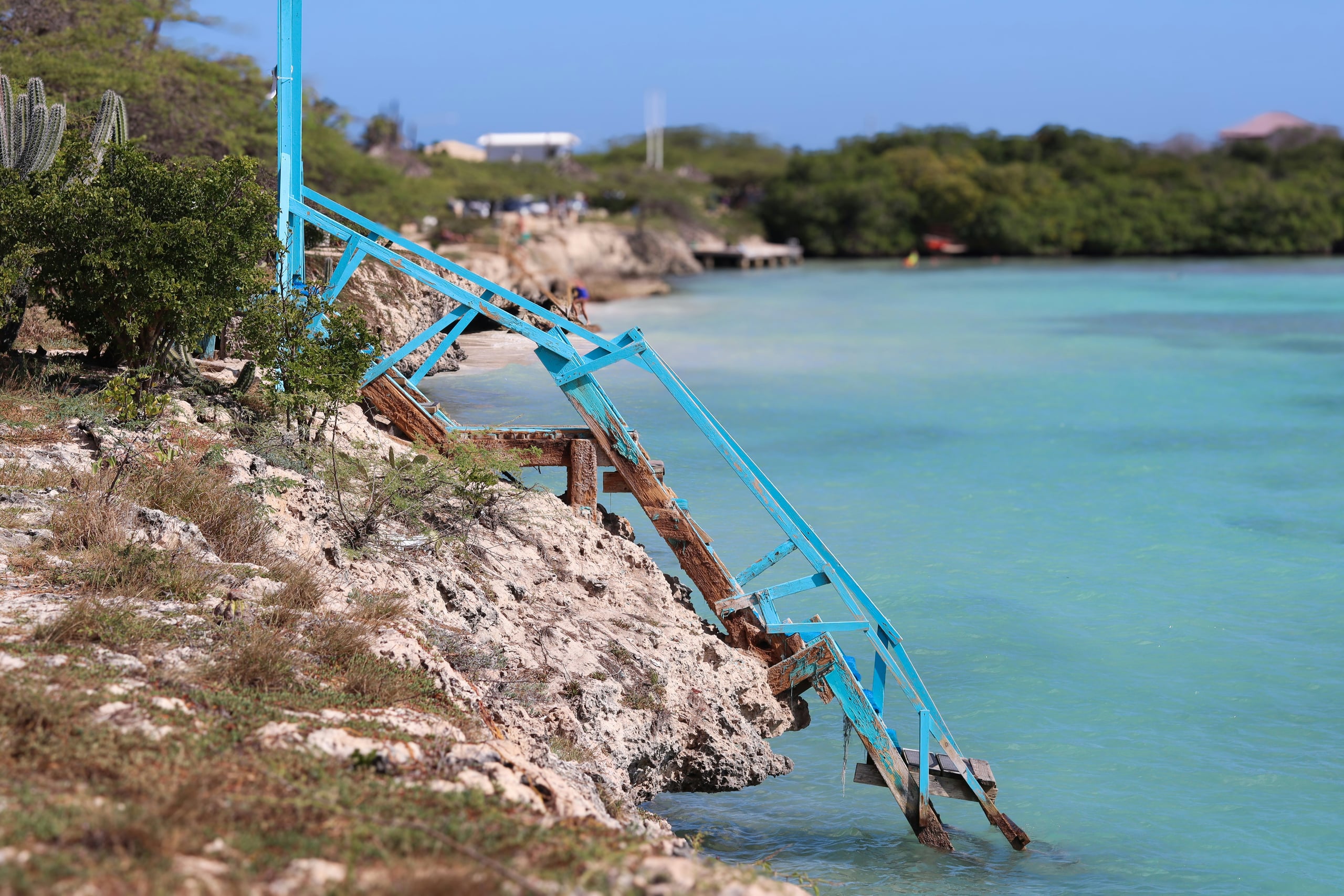 A weathered blue wooden staircase dropping off the rocks into Mangel Halto's turquoise lagoon