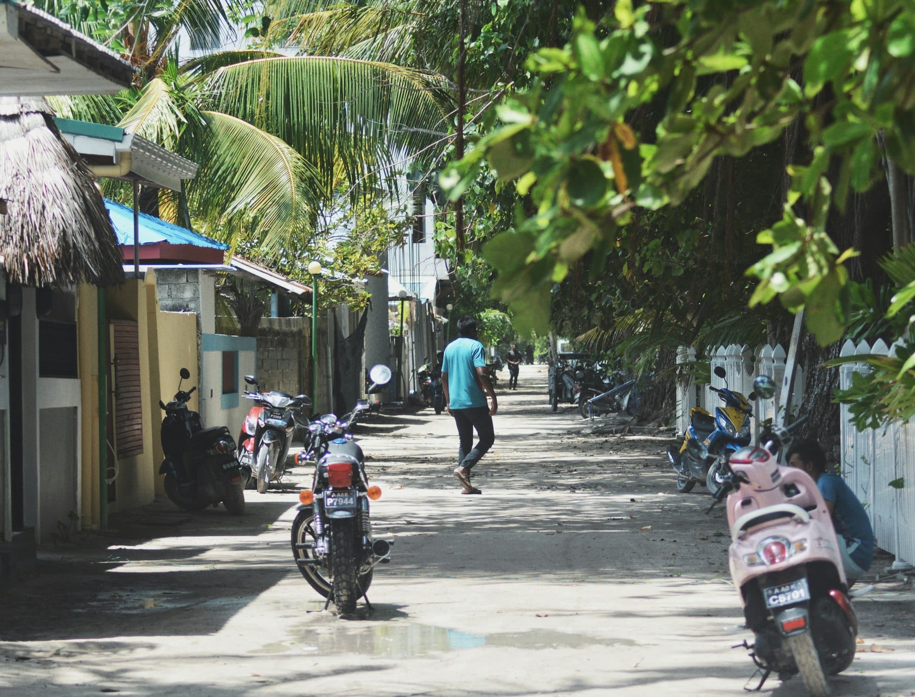A sandy lane on Ukulhas lined with parked motorbikes and scooters, a man walking away between the houses