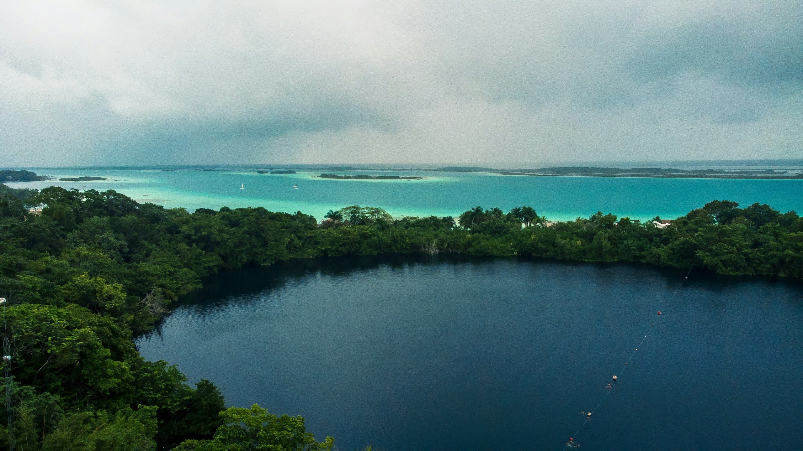 A deep blue circle of water ringed by forest, the pale lagoon running past it to the horizon