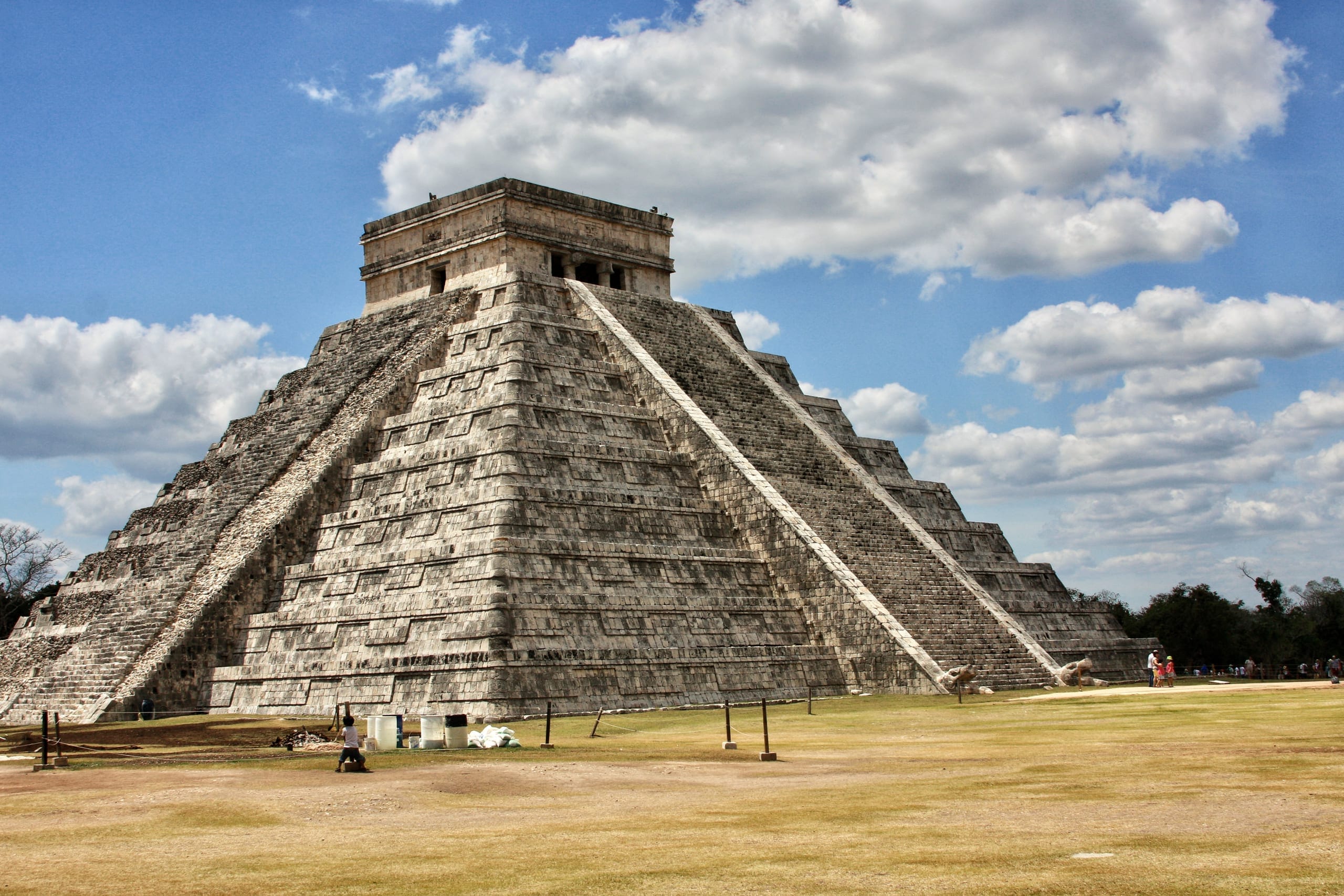 A stepped stone pyramid standing alone on cut grass with a wide stair running up the face nearest you