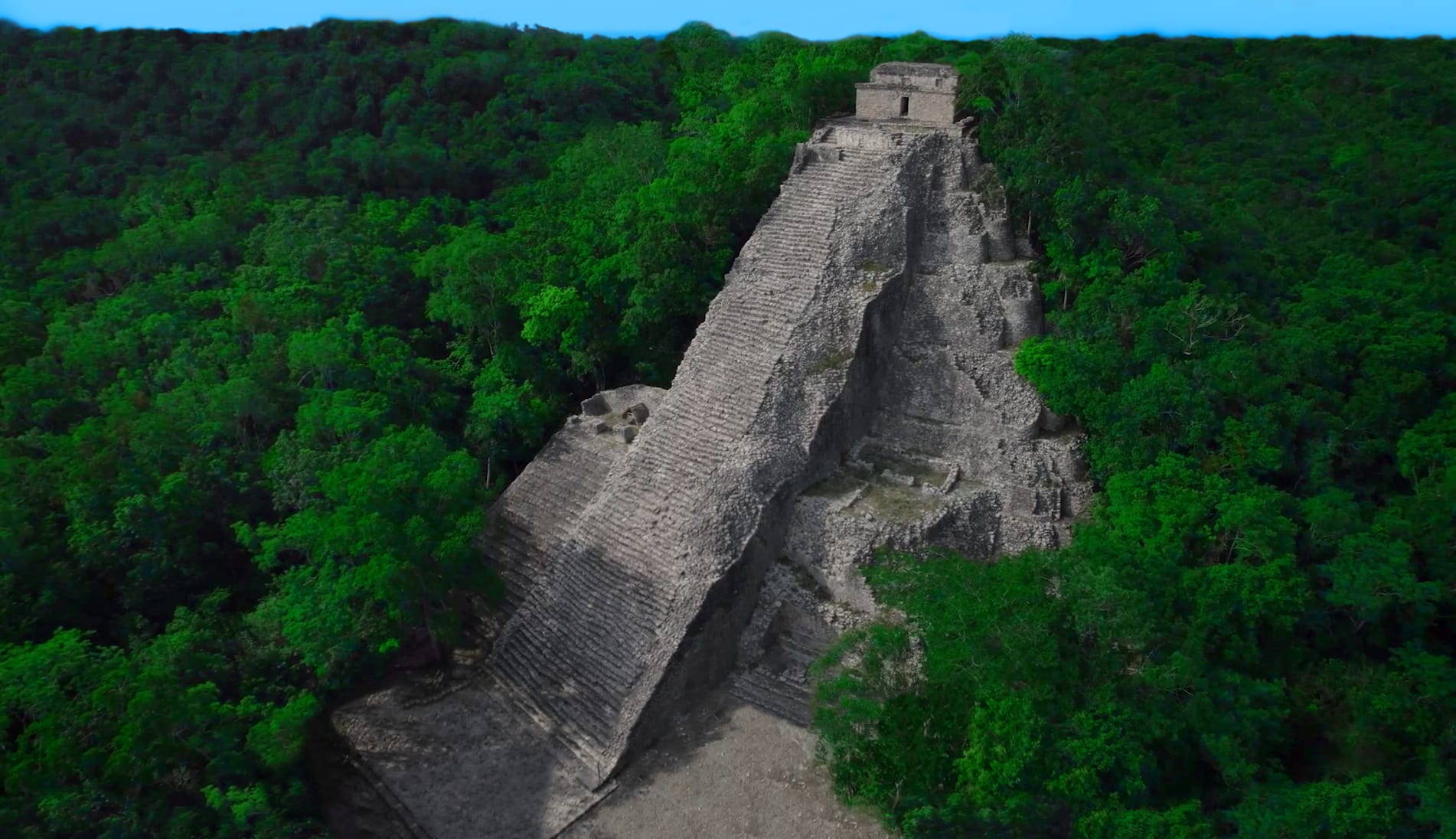 A steep stone pyramid rising out of unbroken jungle, seen from the air
