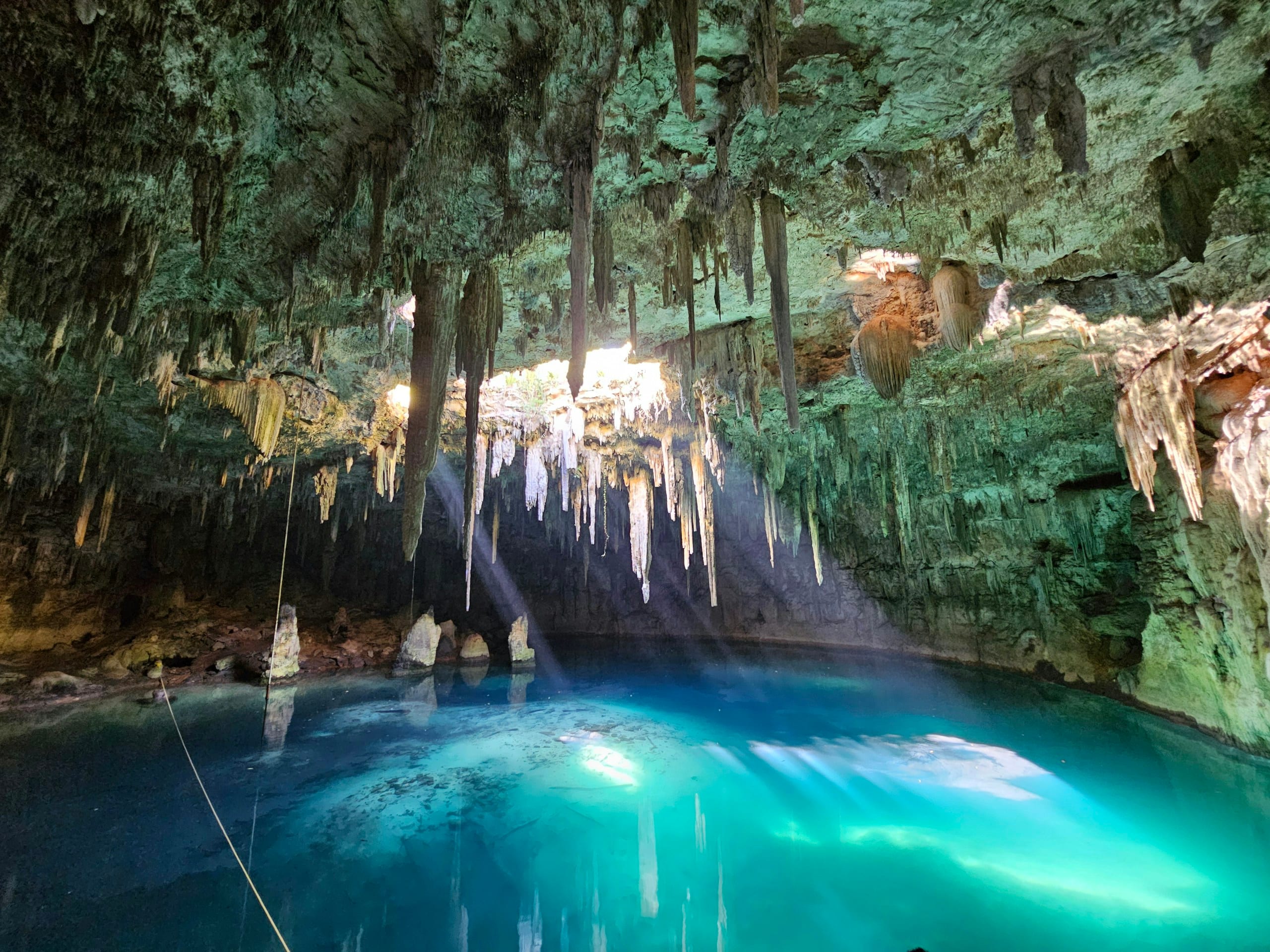 Stalactites hanging over a lit blue pool inside a cavern