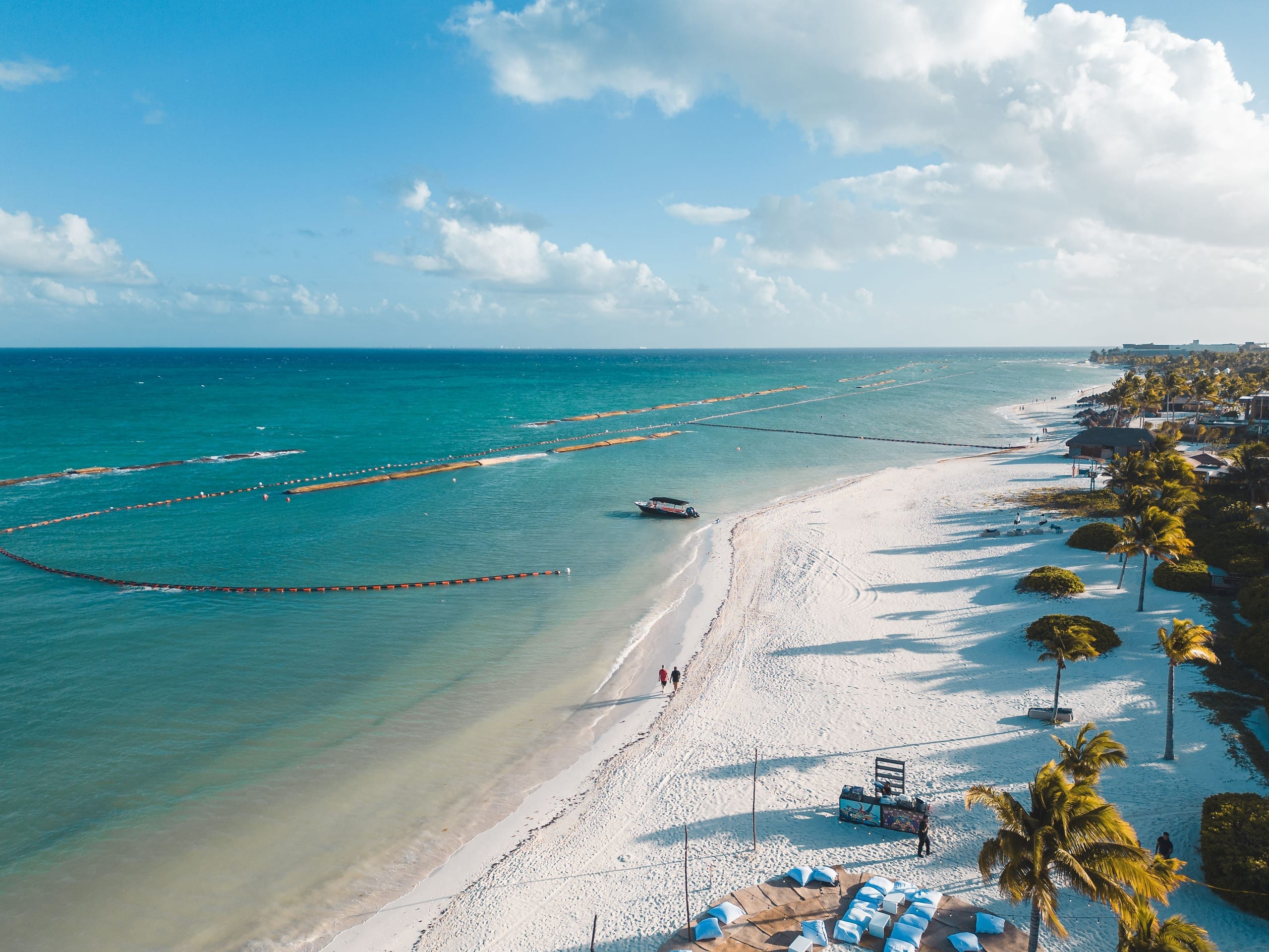 A long beach seen from the air, palms along the sand and a rope line running out into the shallows