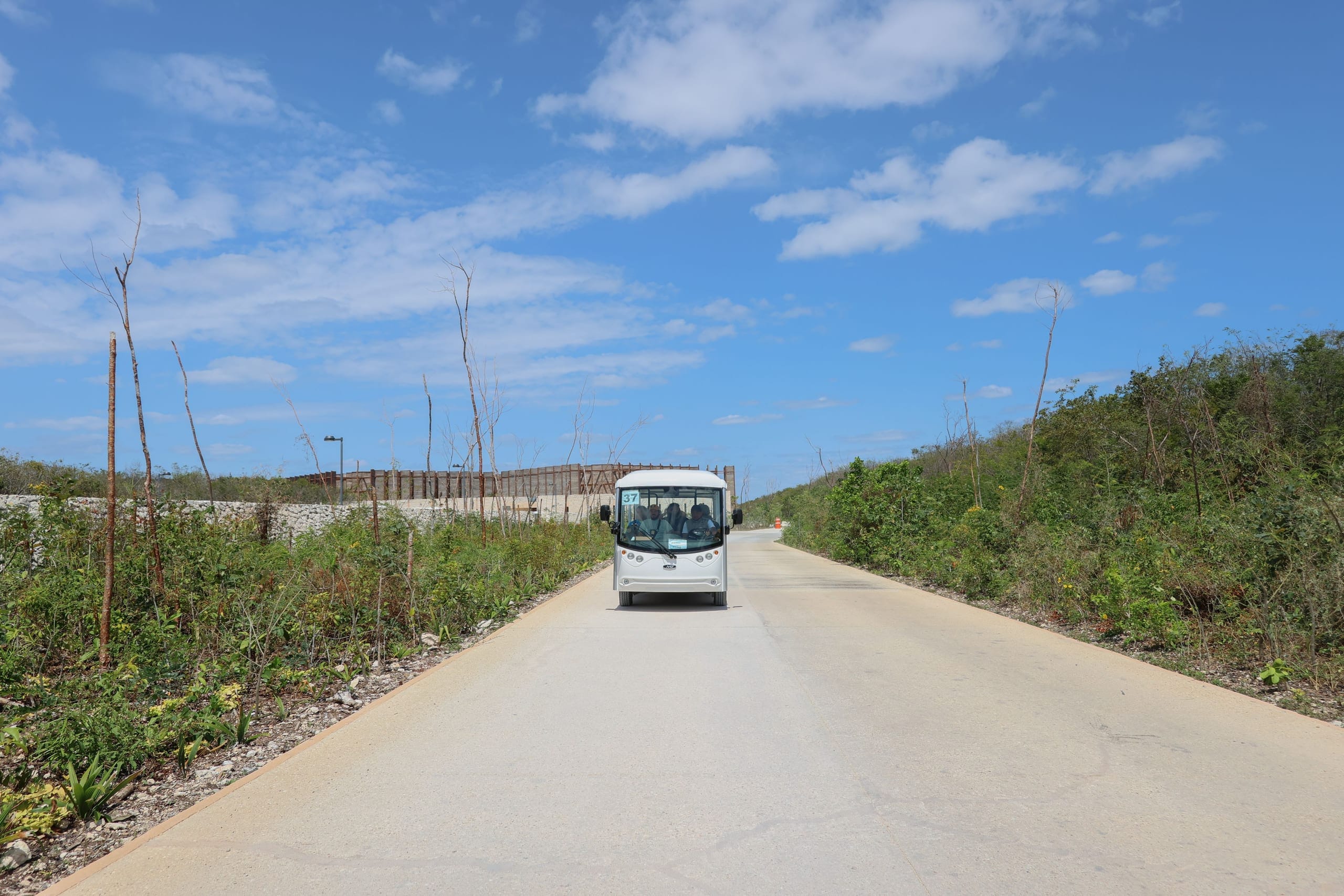 A small white shuttle coming down an empty two lane road through low green scrub